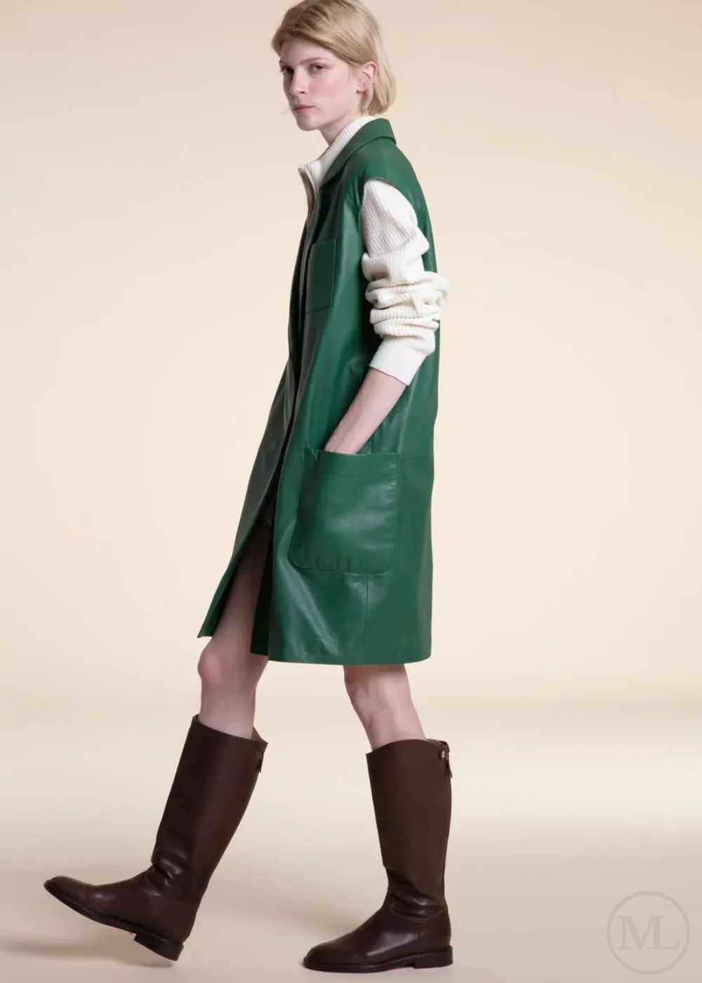 Woman wearing a Emerald green leather coat and brown boots on a beige background