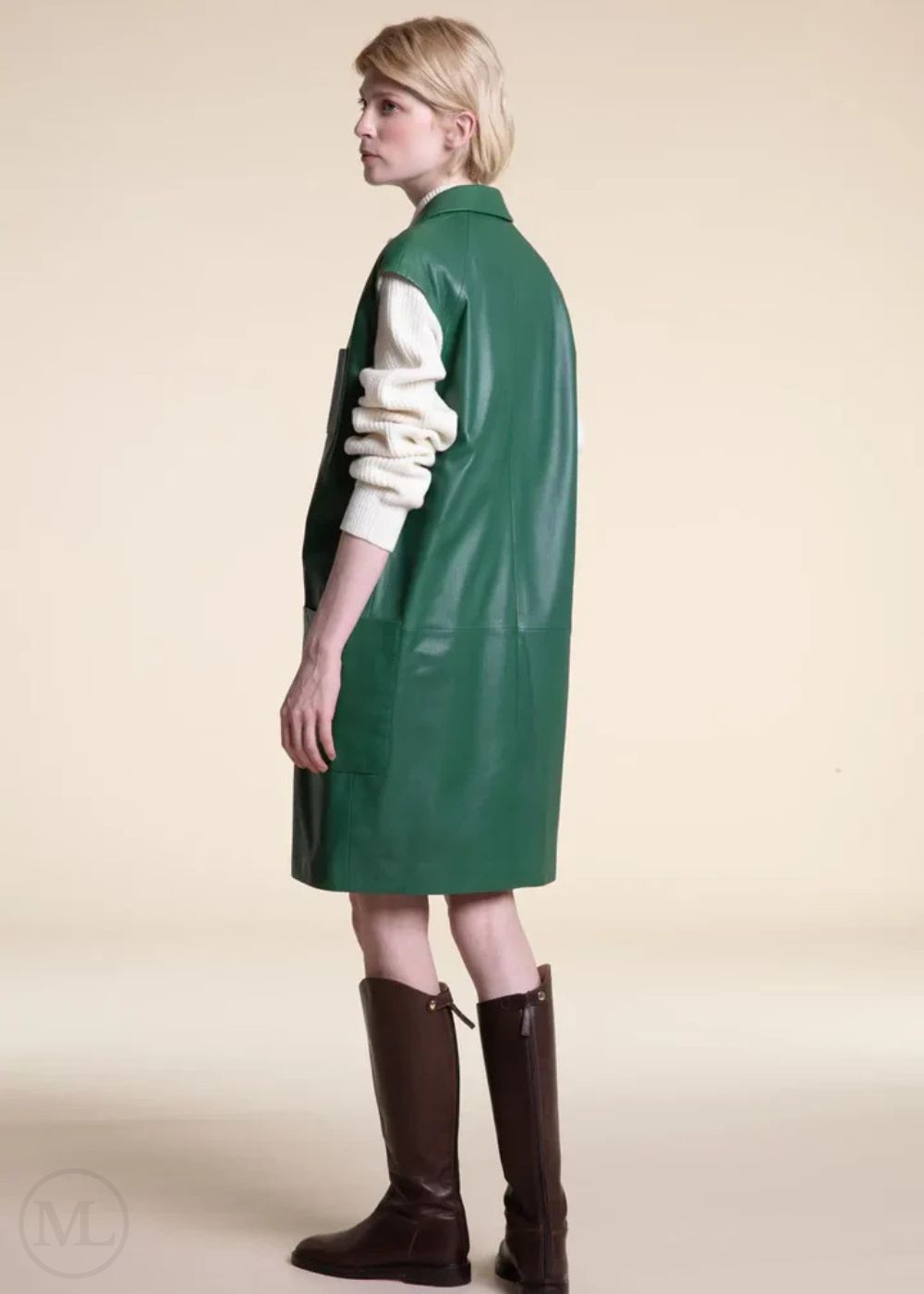 Women wearing a emerald green dress with a white sweater and brown boots on a beige background