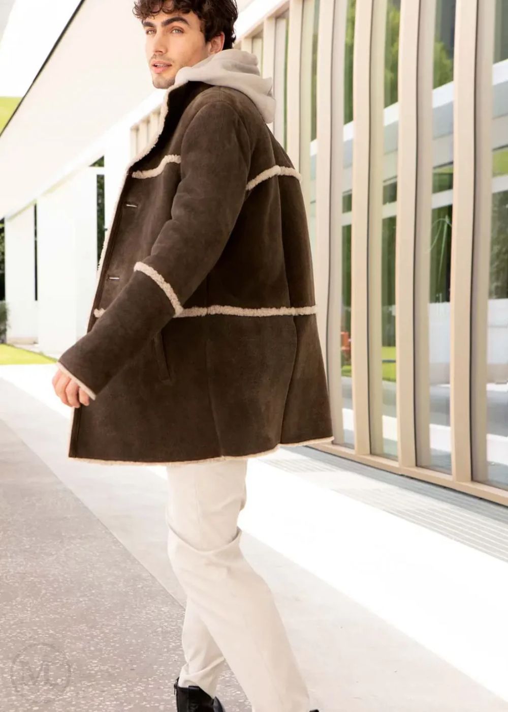 Man wearing a brown suede coat with white trim walking outdoors.
