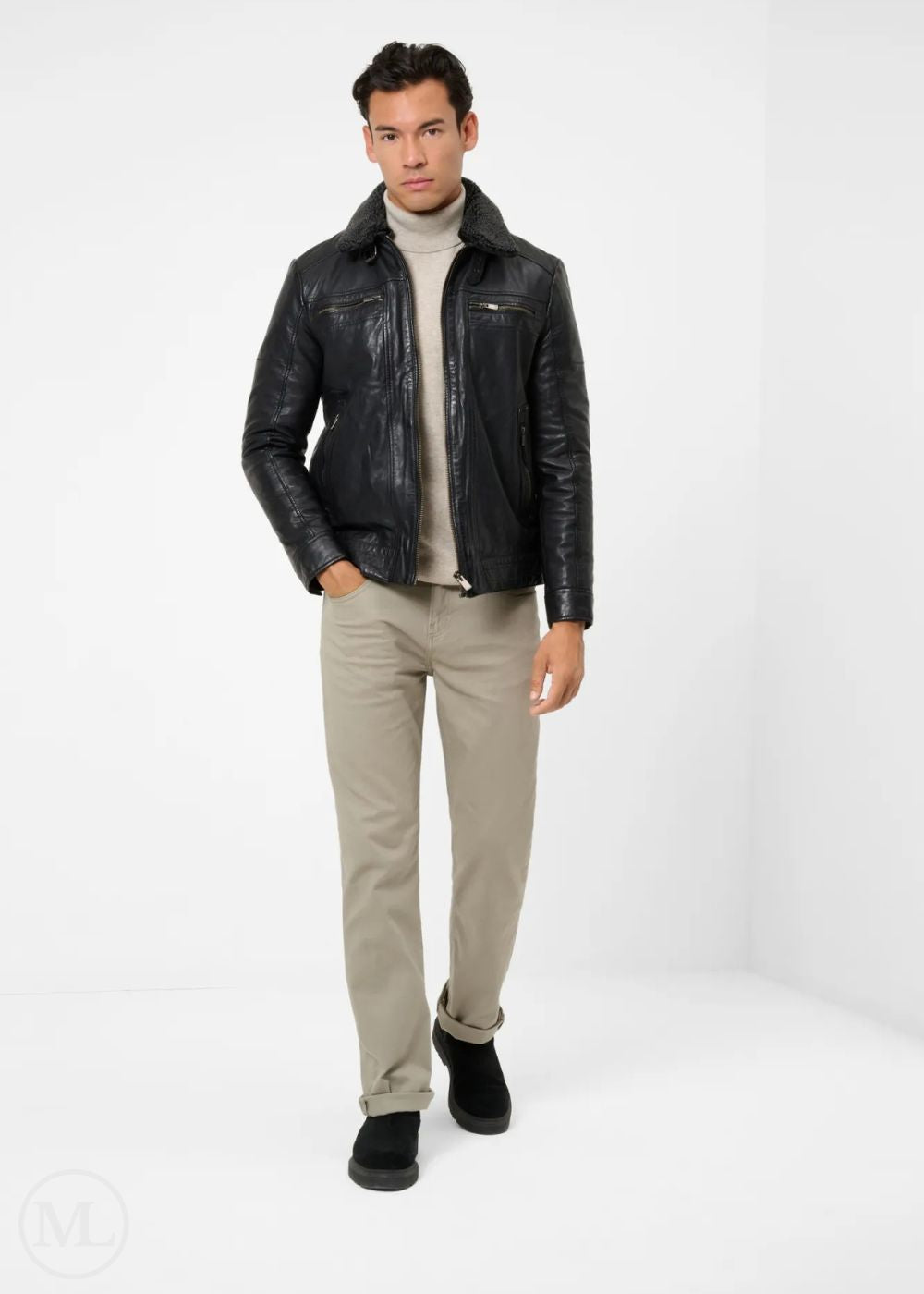 Man wearing a black leather jacket, beige sweater, and pants on a white background