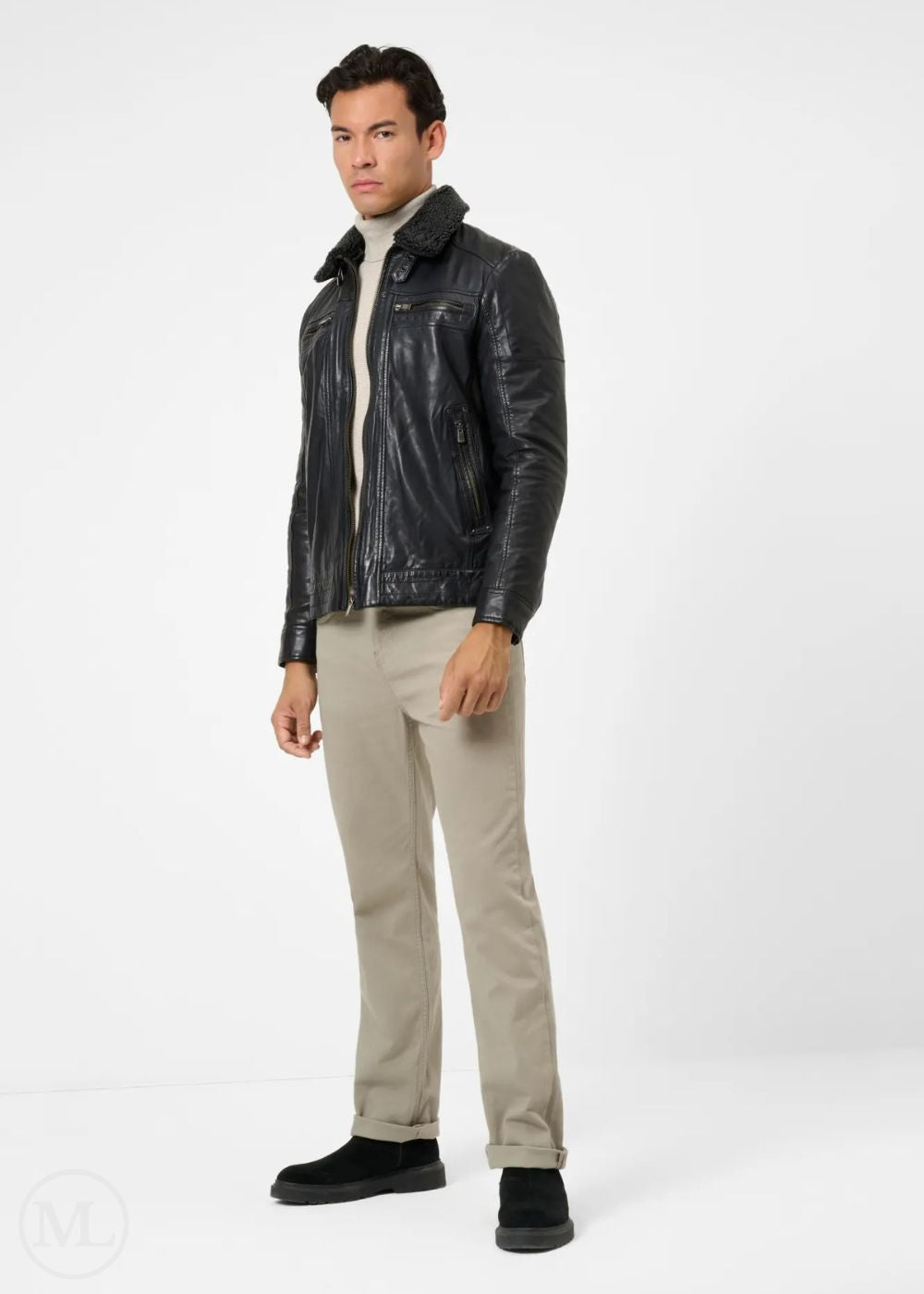 Man wearing a black leather jacket, white turtleneck, beige pants, and black shoes on a white background