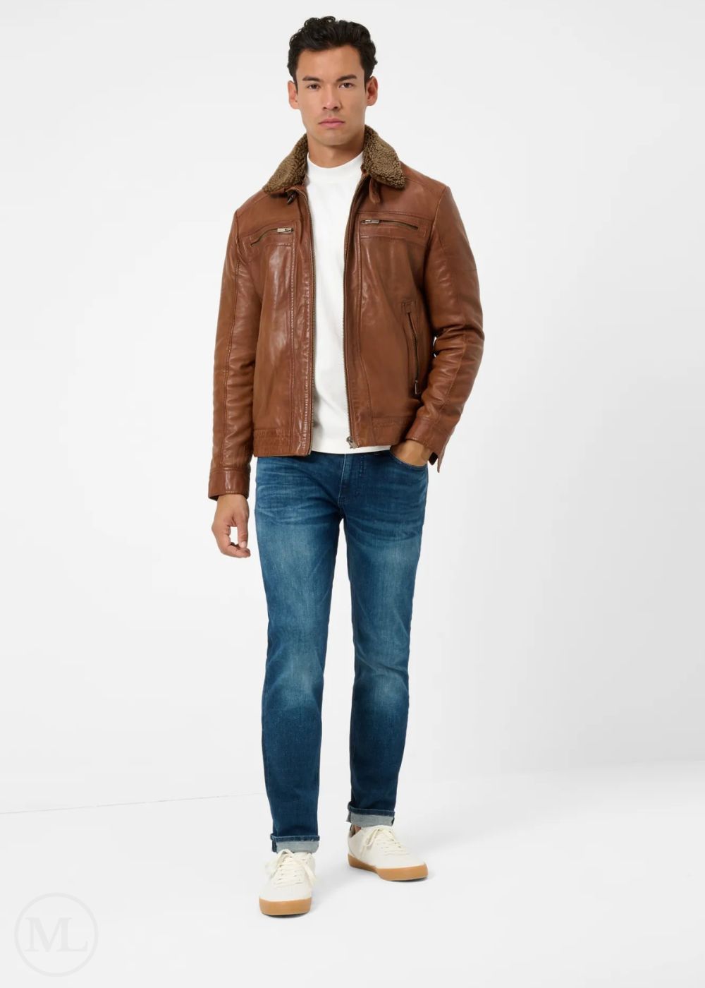 Man wearing a cognac brown leather jacket, white shirt, blue jeans, and white sneakers on a white background
