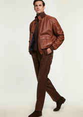 Man wearing a cognac leather bomber jacket and pants on a white background
