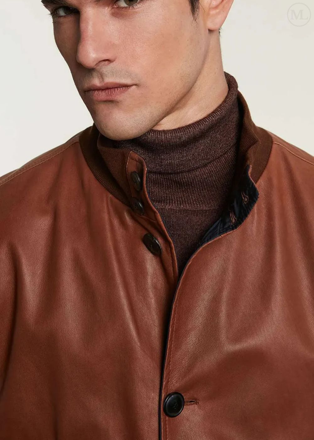 Man wearing a camel leather bomber jacket over a brown turtleneck sweater on a plain background