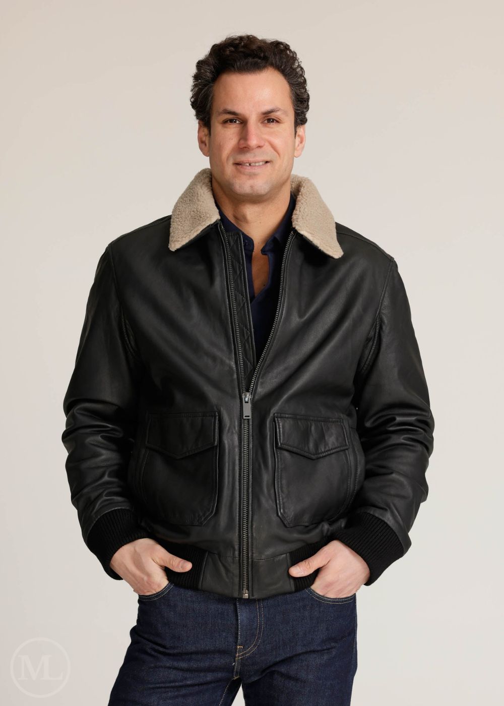 Man wearing a black leather bomber jacket with beige lining on a plain background