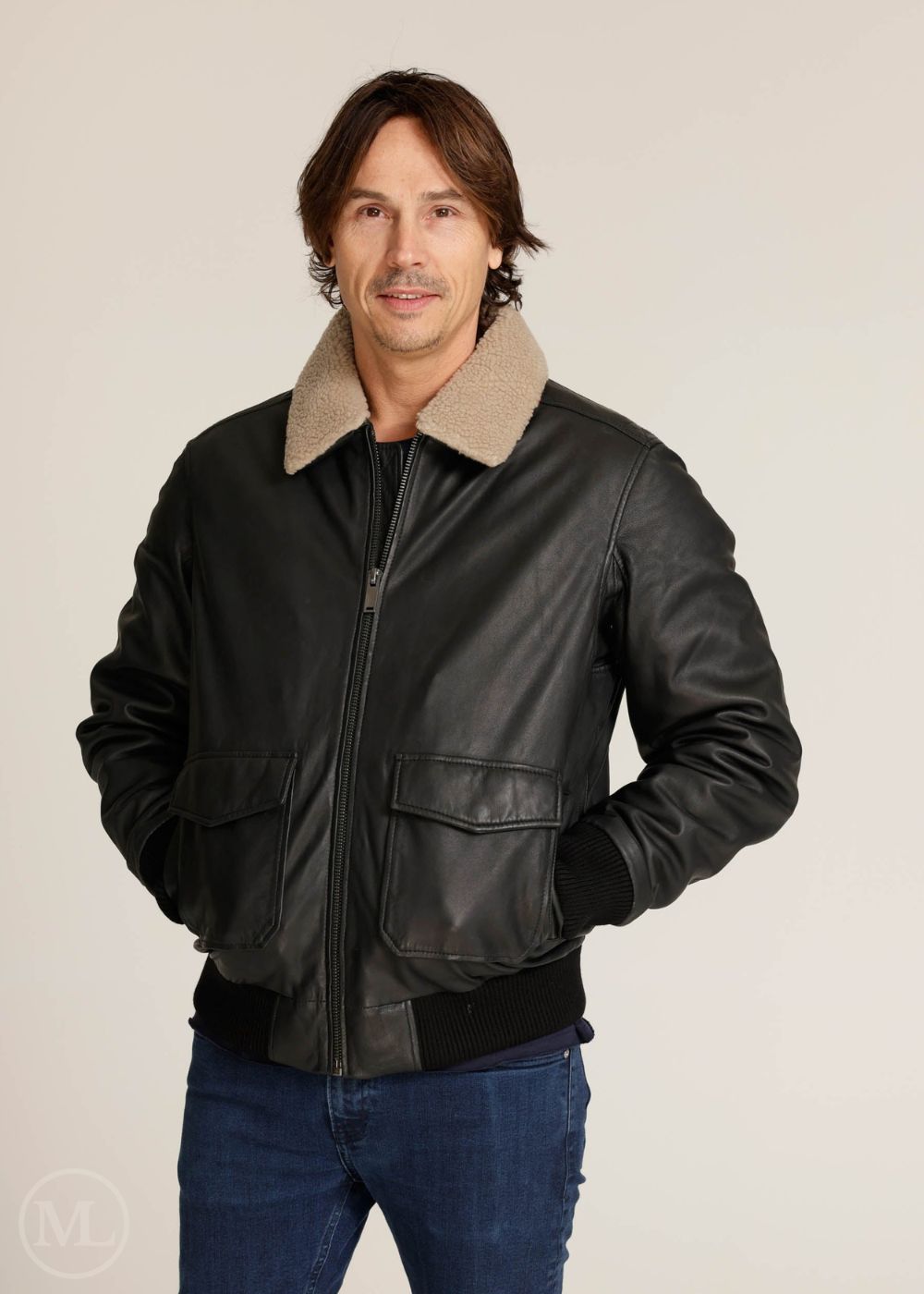 Man wearing a black bomber leather jacket with a beige collar on a plain background