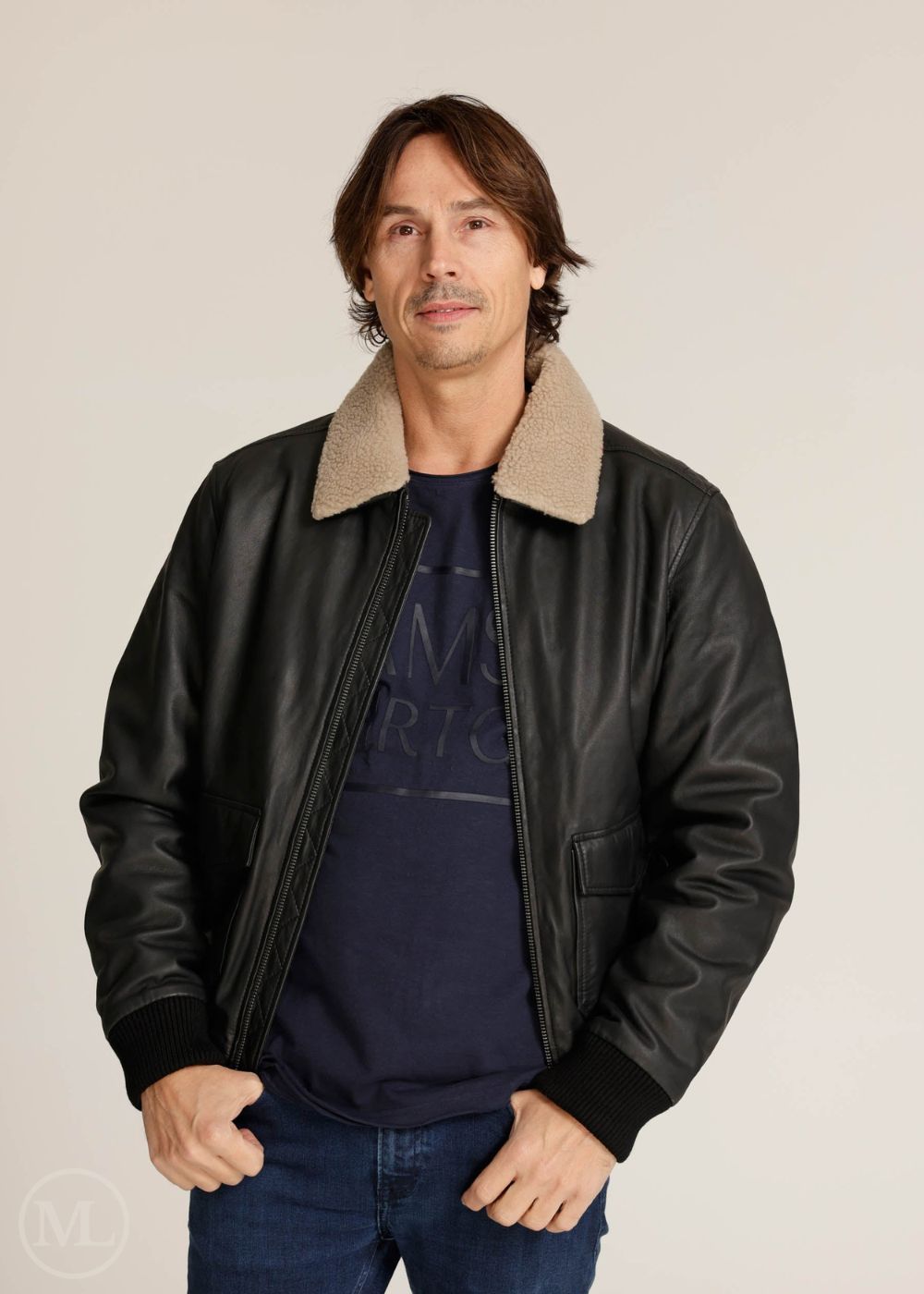 Man wearing a black leather bomber jacket with beige collar on a plain background