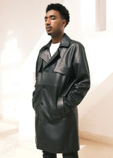Man wearing a black leather trench coat in a neutral setting