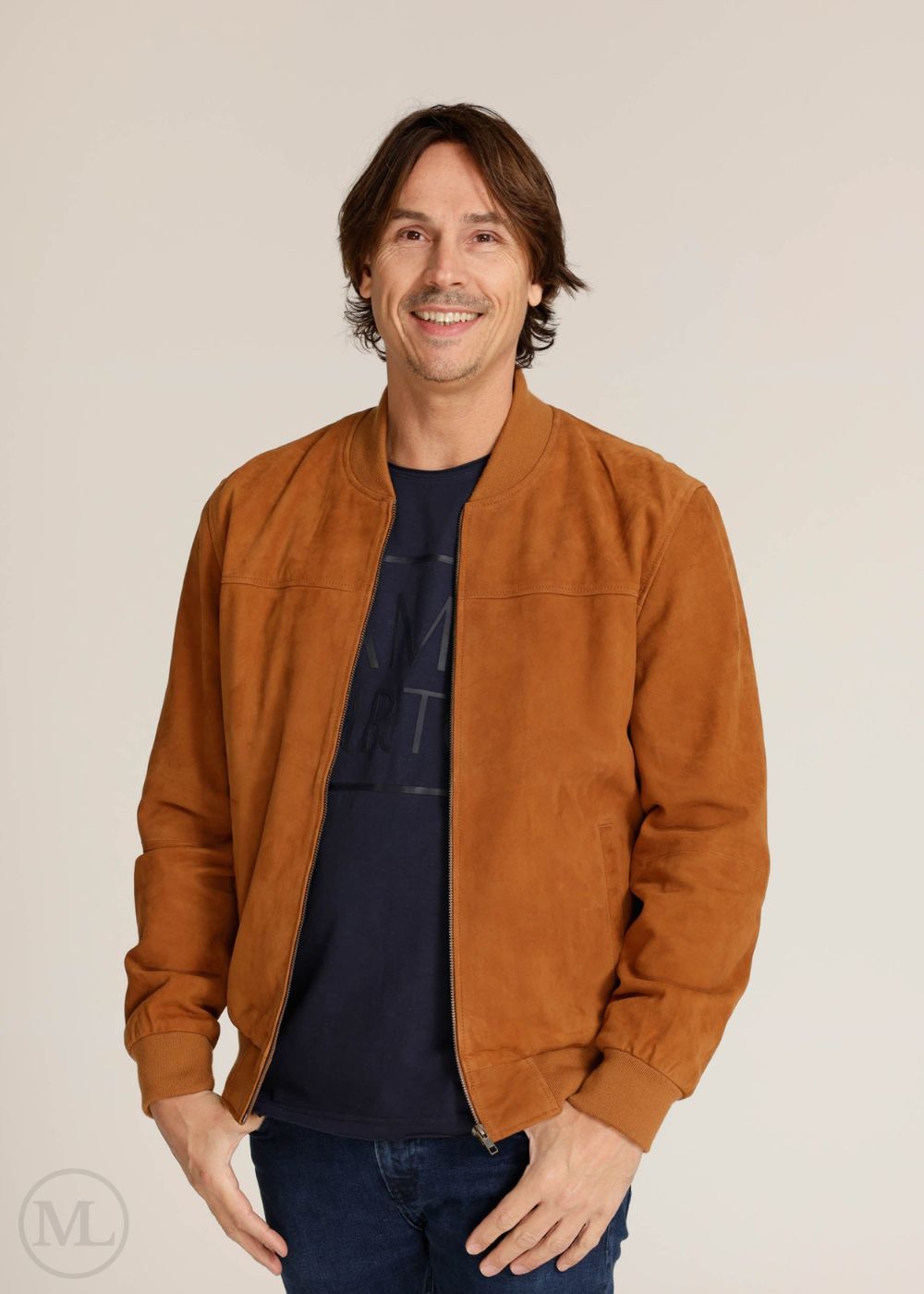 Man wearing a cognac brown suede jacket over a dark shirt on a beige background