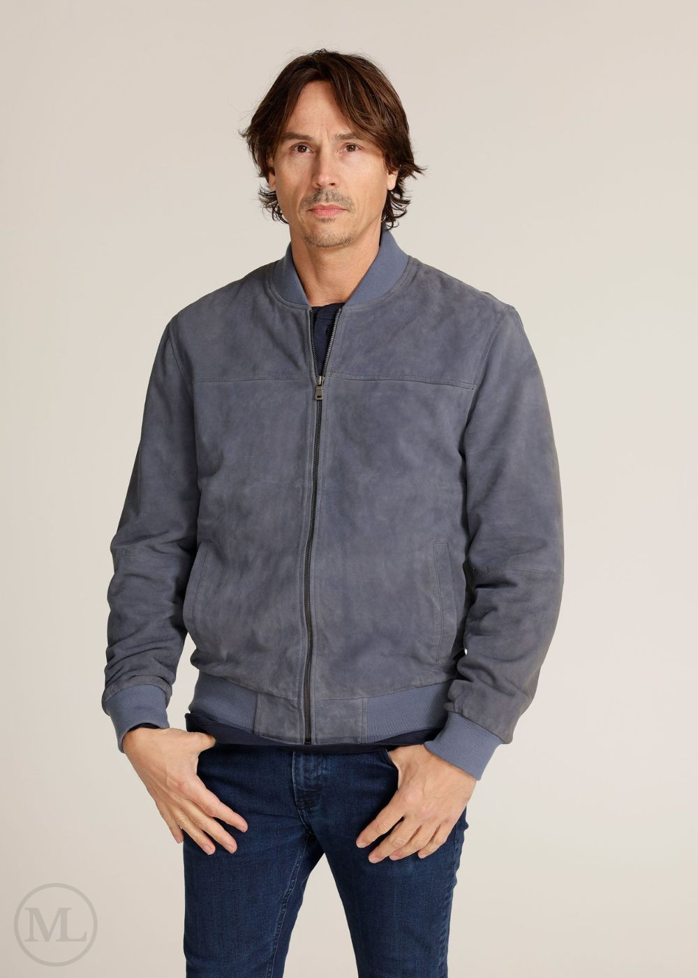 Man wearing a navy suede jacket and blue jeans against a plain background