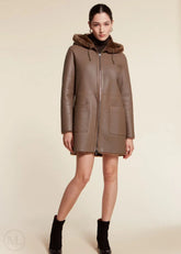 Brown shearling wool leather coat with fur hood worn by a woman on a beige background