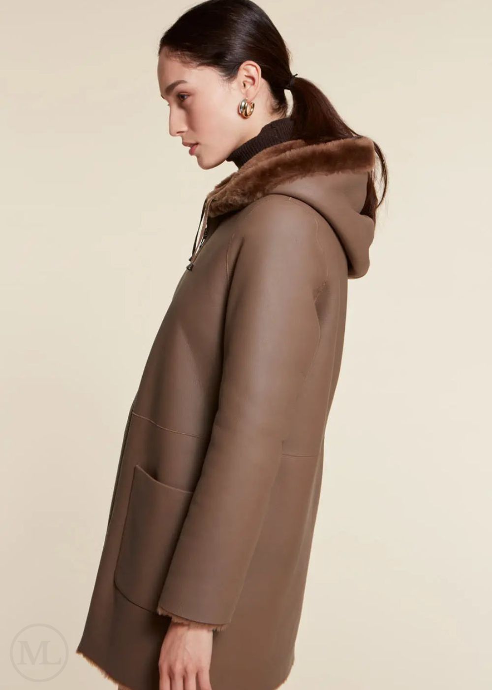 Brown shearling wool coat with fur hood worn by a woman on a beige background