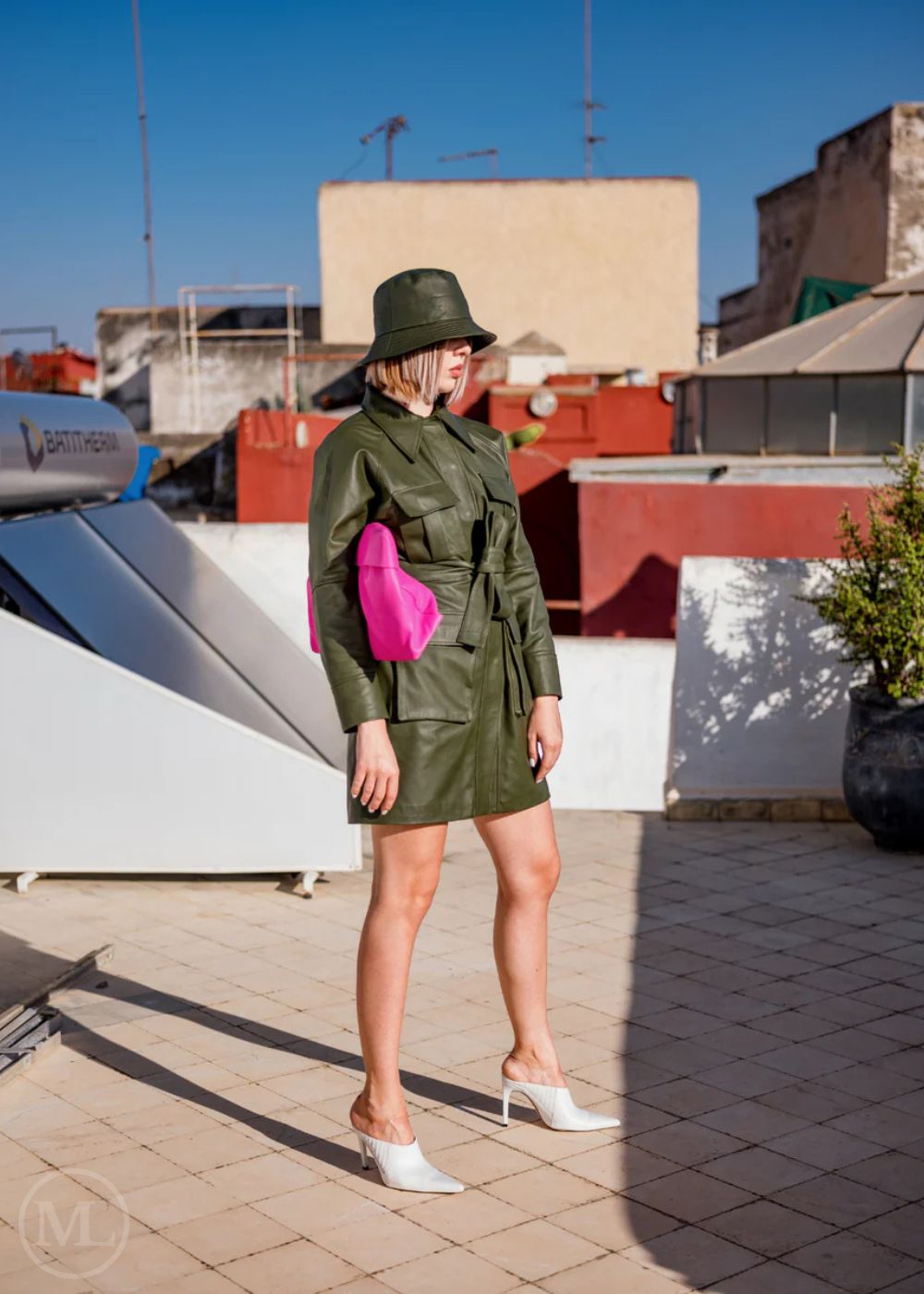 Woman Wearing a Olive green Leather coat and hat standing on a rooftop with buildings in the background
