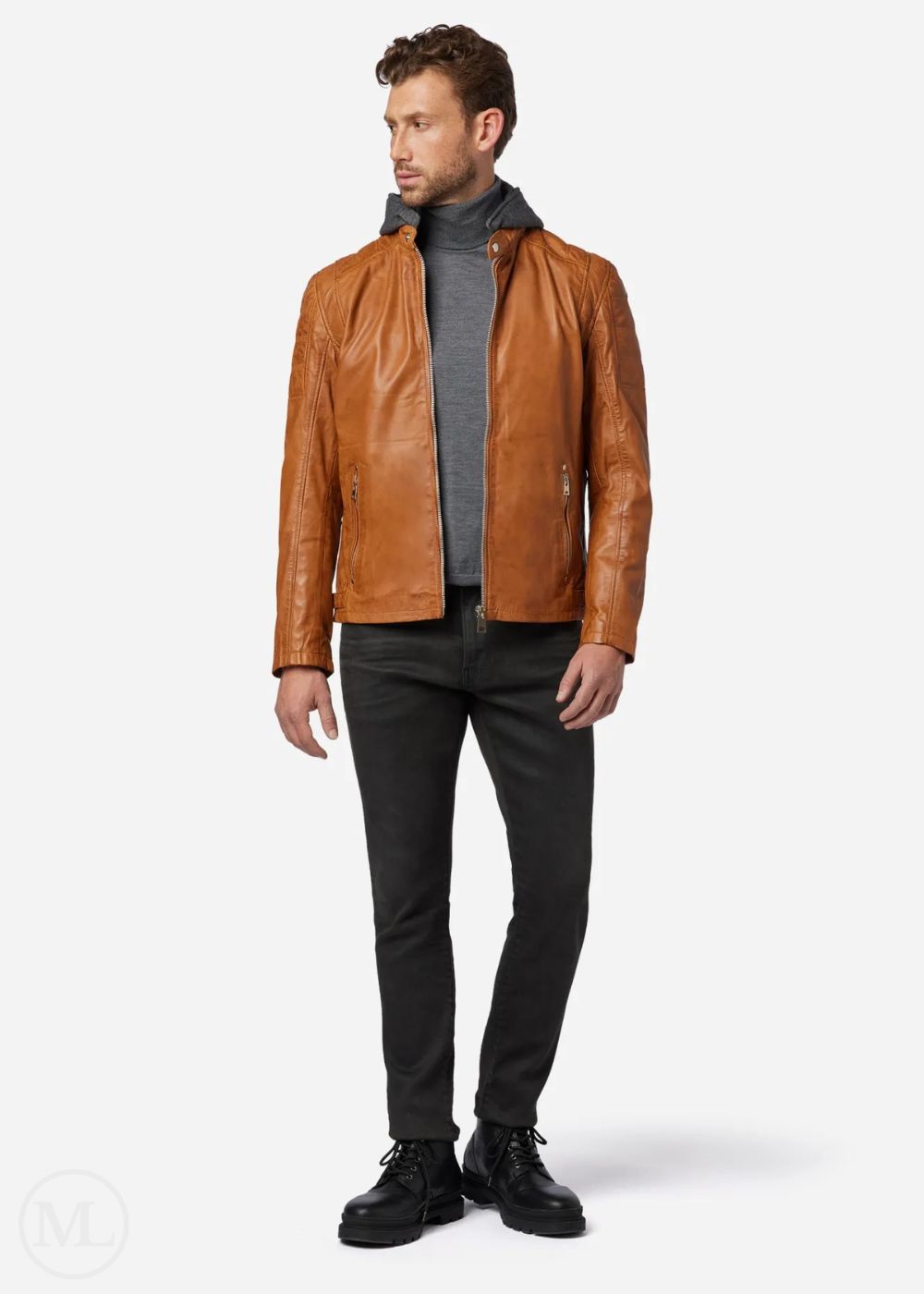 Man wearing a cognac brown leather biker jacket, gray sweater, black pants, and black shoes on a white background