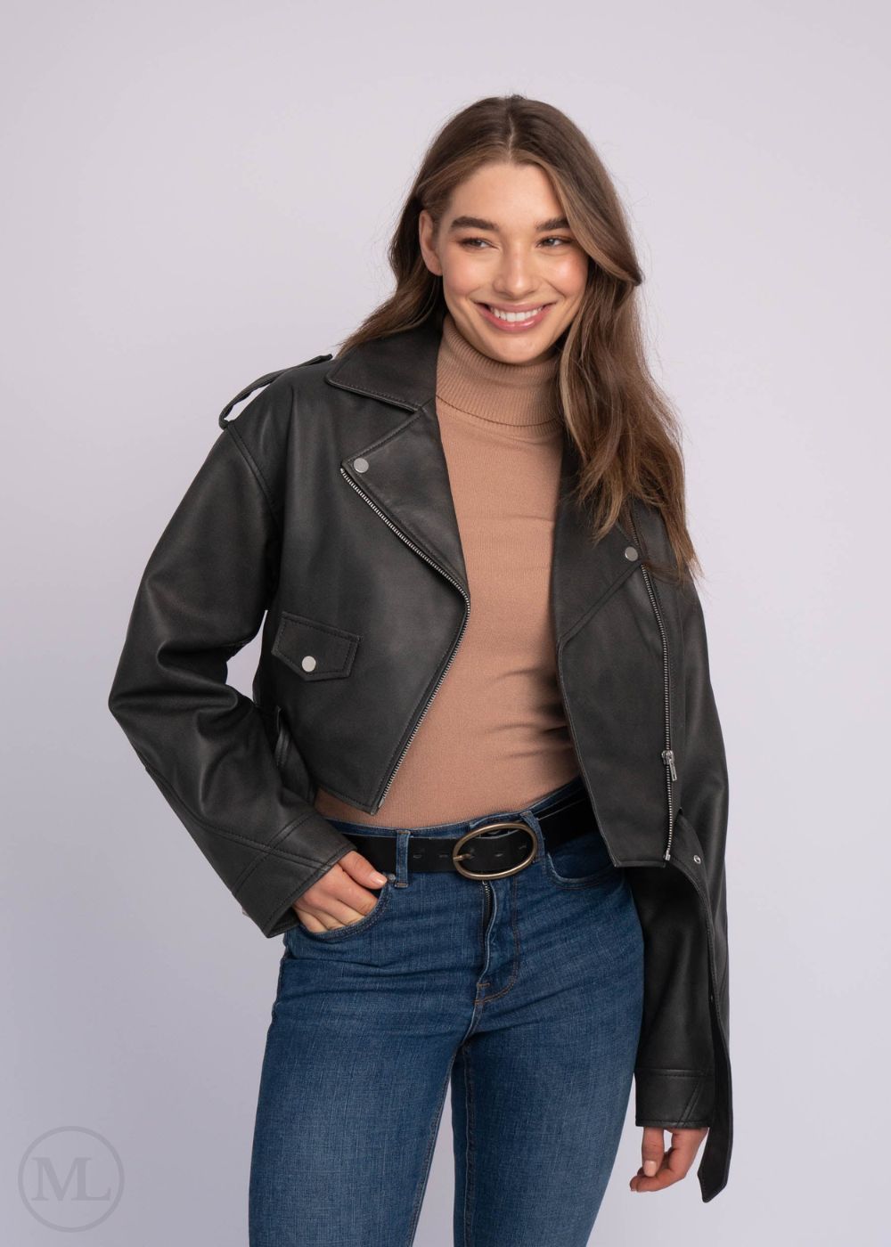 Femme portant une veste en cuir noire, un col roulé beige et un jean bleu sur fond gris clair