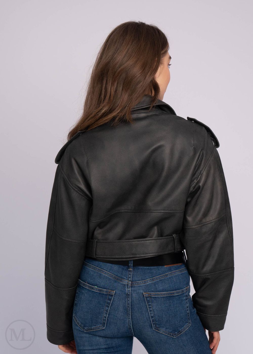 Femme portant une veste en cuir noire et un jean bleu sur fond uni