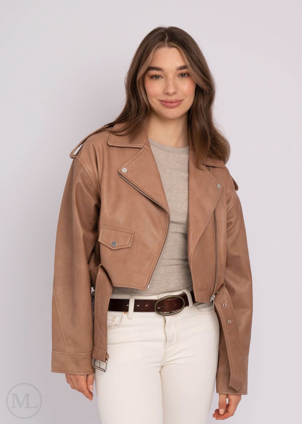 Woman wearing a taupe leather jacket over a gray top and white pants on a plain background