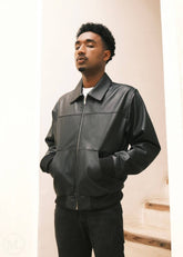 Man wearing a black leather bomber jacket in shirt collar against a neutral background