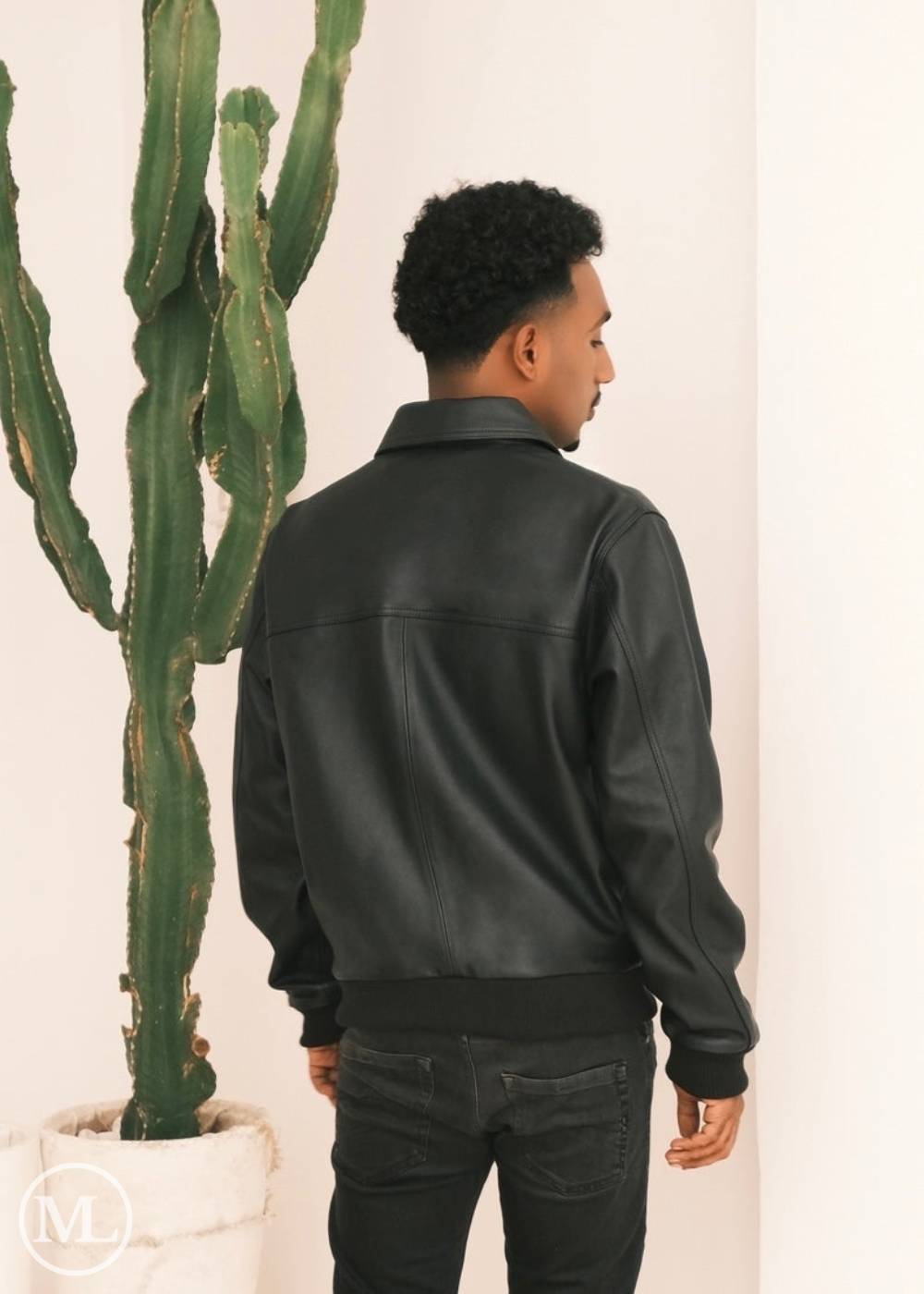 Person wearing a black leather bomber jacket with shirt collar standing next to a cactus plant. back view