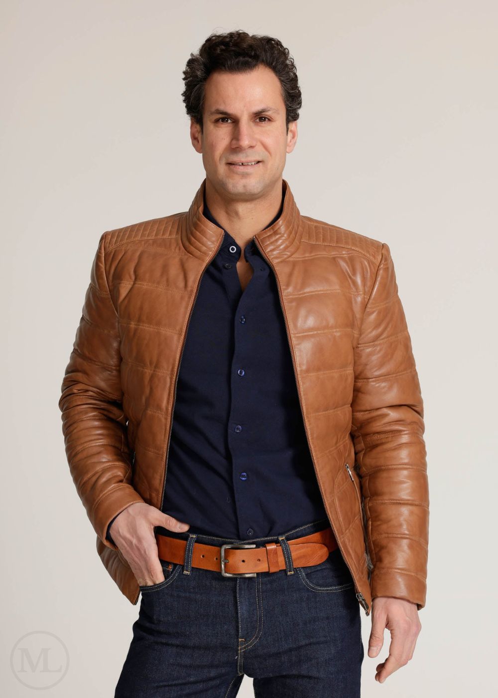Man wearing a cognac brown leather jacket over a dark shirt on a plain background