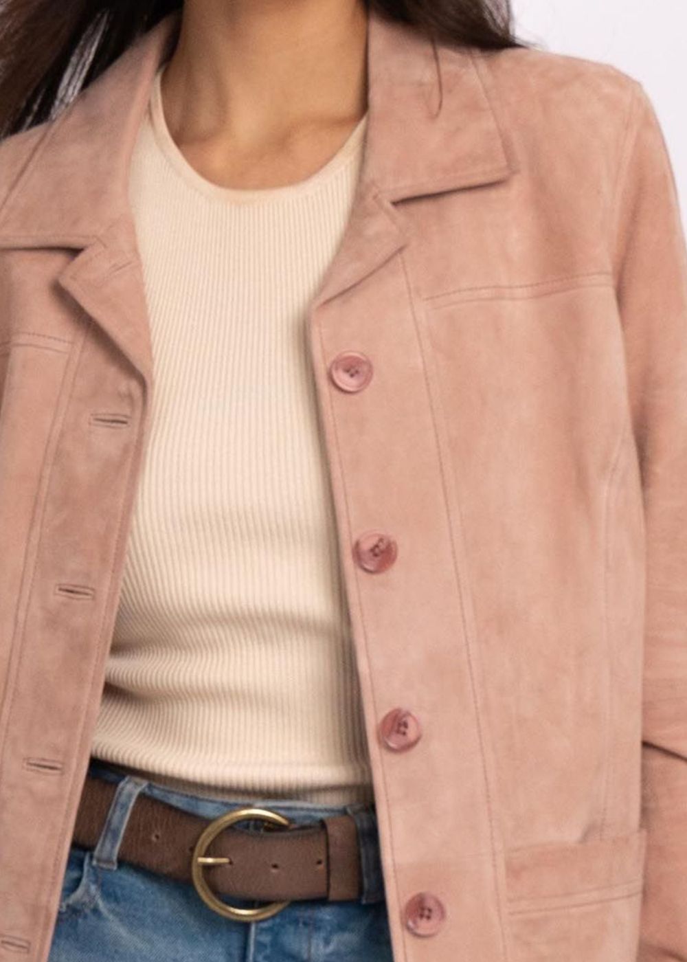 Femme portant un manteau en cuir rose sur un pull crème avec un jean bleu et une ceinture marron.