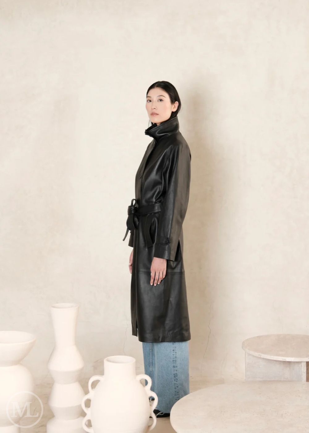 women wearing a black leather trench coat, standing in side postiion, to show left side of the coat