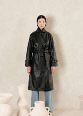 women wearing a black leather trench coat with belted waist and a beige background