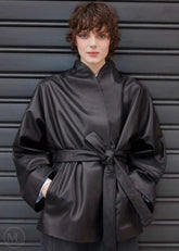 Woman wearing a black belted wrap leather blazer coat against a gray background