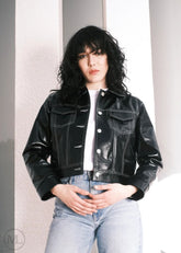 Women wearing a Cropped black leather Trucker jacket and light blue jeans against a neutral background