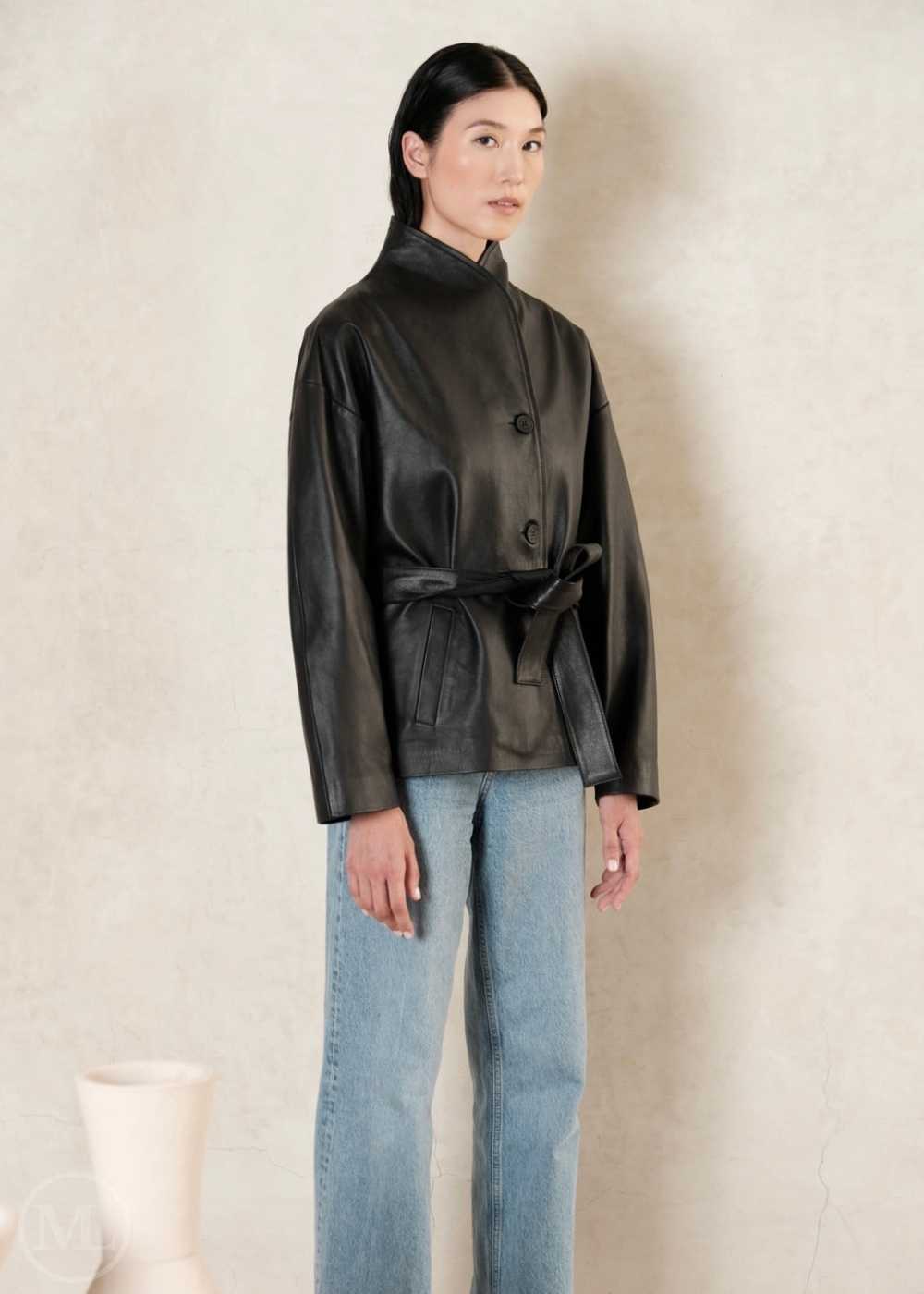 Woman wearing a black leather coat and light blue jeans against a plain background