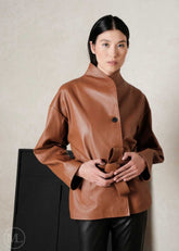 Woman wearing a brown leather coat style jacket against a plain background