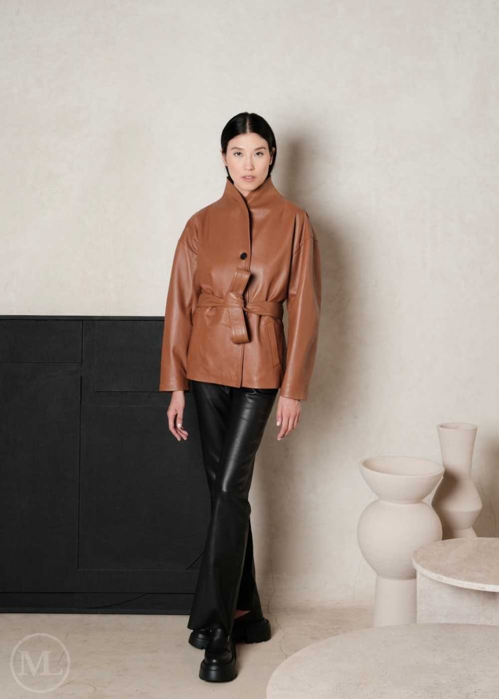 Woman wearing a brown leather coat and black leather pants in a minimalistic setting