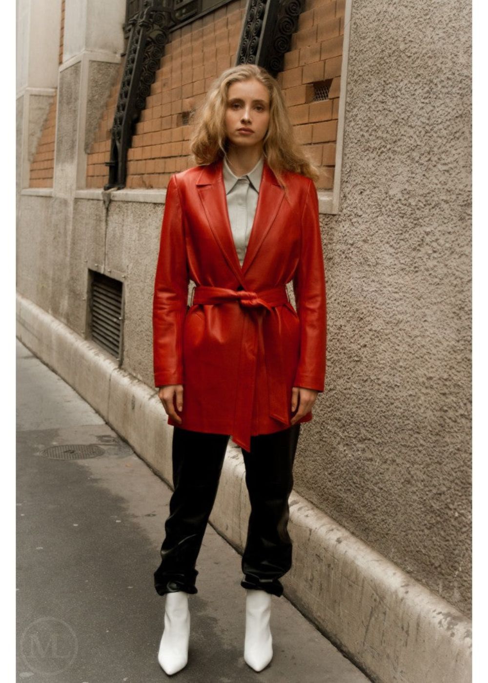 Woman wearing a red leather blazer coat standing on a street corner.