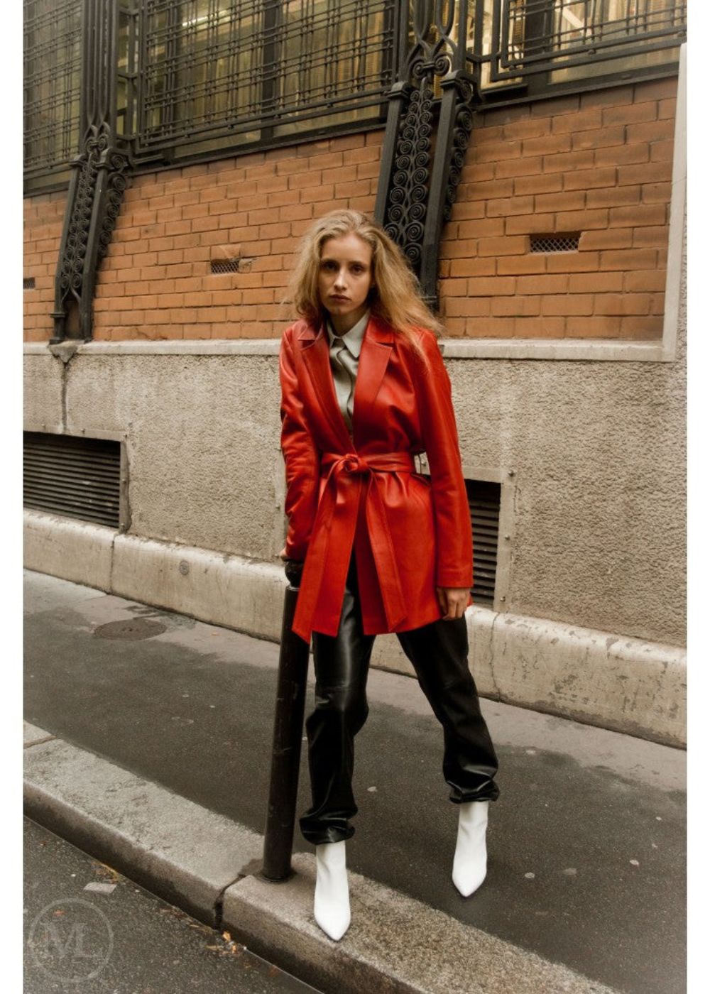 Woman in a red leather blazer coat standing on a city street.