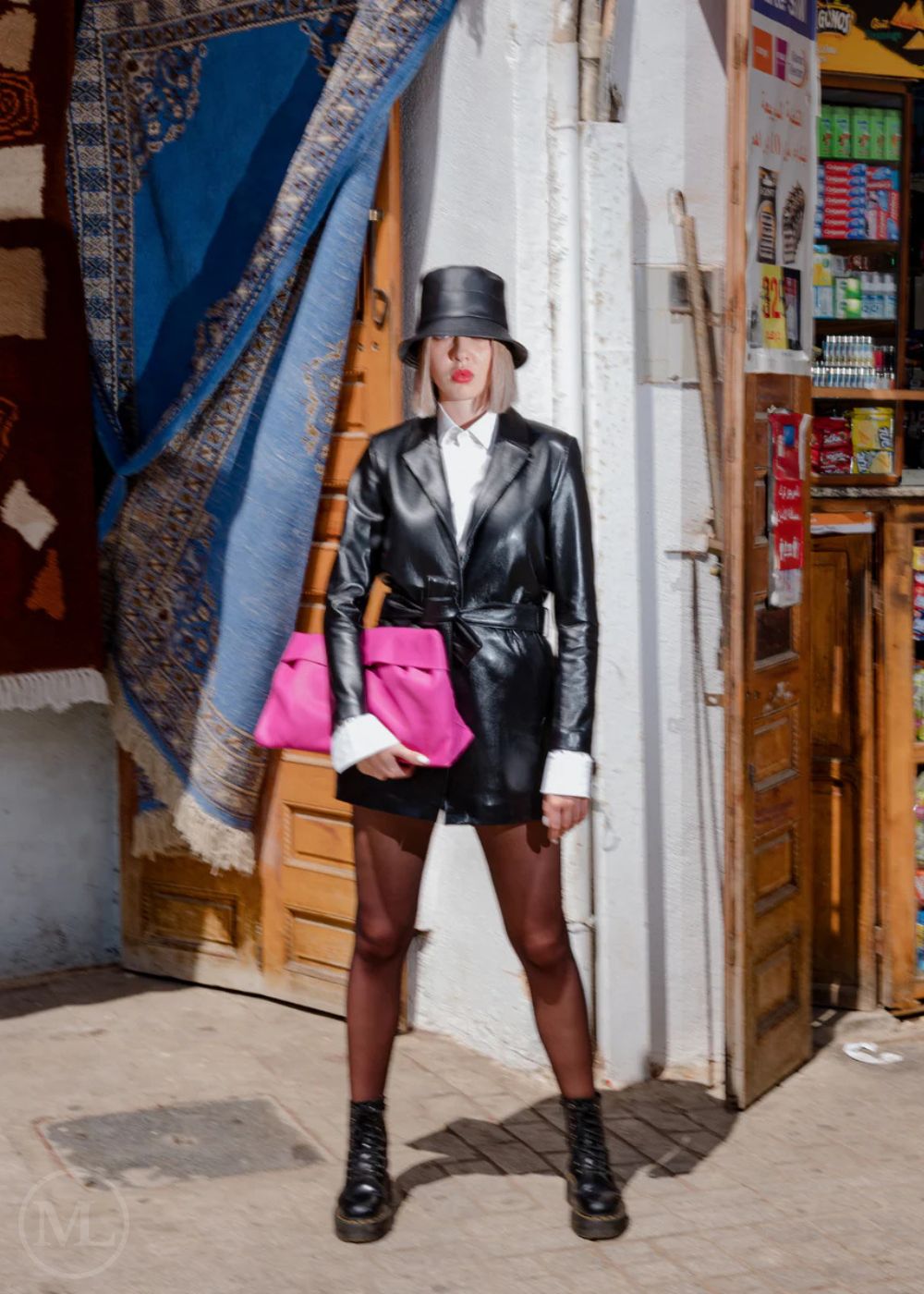 Women wearing a black leather blazer coat outfit with a pink clutch in an urban setting