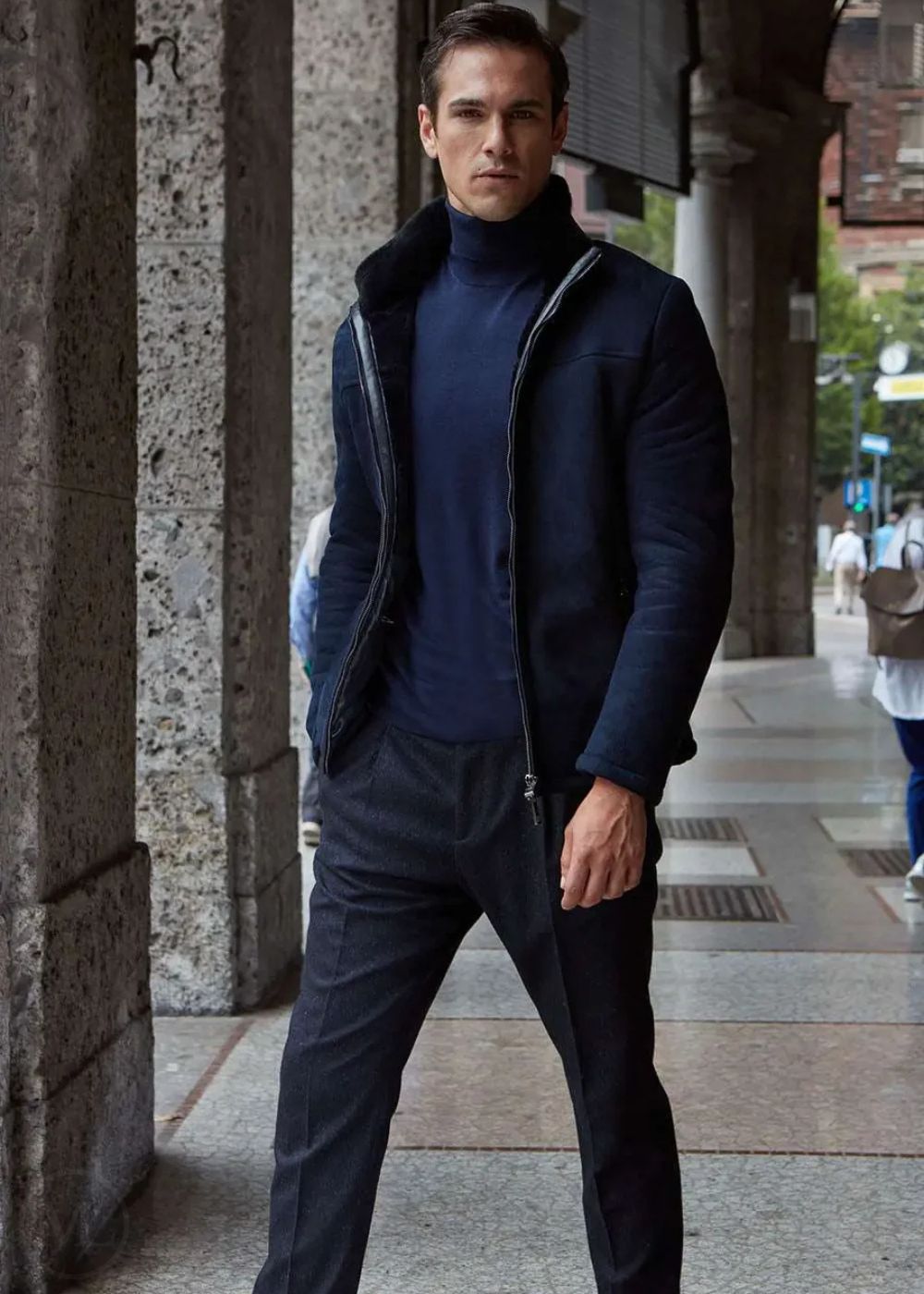 Man wearing a Navy blue jacket and pants standing in an urban setting