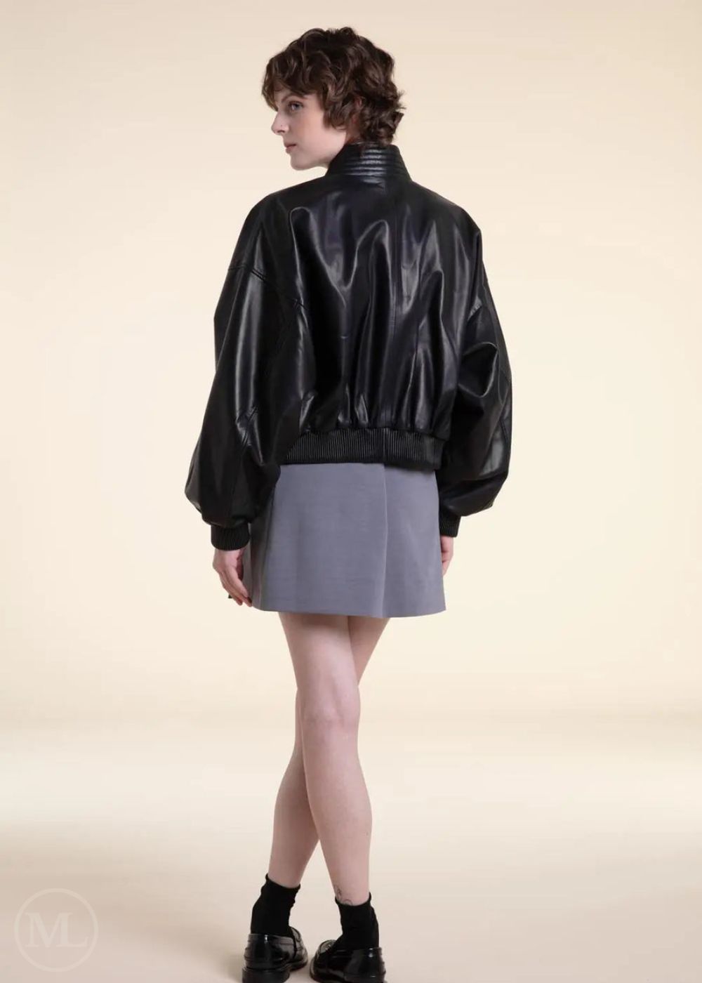 Woman wearing a black leather bomber jacket and gray skirt on a beige background