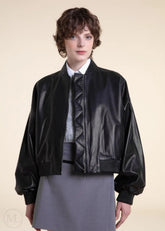 woman wearing a black leather bomber jacket on a beige background