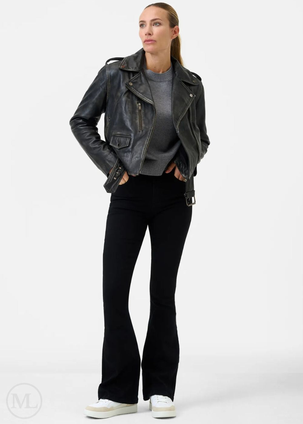 Woman wearing a black leather biker jacket, gray shirt, and black pants on a white background