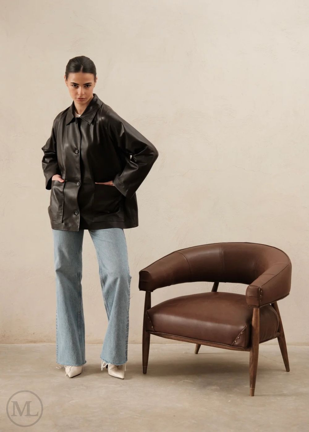 Woman wearing a dark brown leather trucker jacket against a beige background