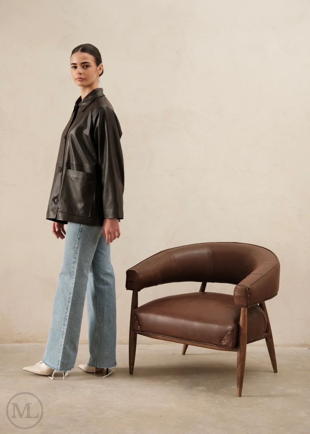 Woman wearing a dark brown leather trucker jacket against a beige background