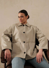Women wearing a lvory leather blazer coat sitting on a chair against a plain background