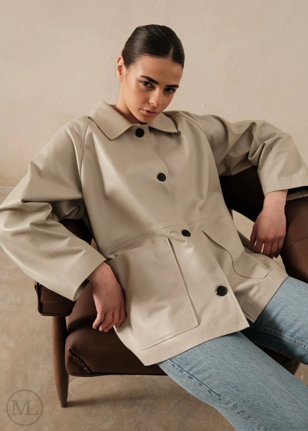 Woman wearing a lvory leather blazer jacket sitting on a chair against a neutral background