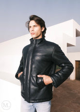 Man wearing a black leather down jacket standing outdoors with a modern building in the background