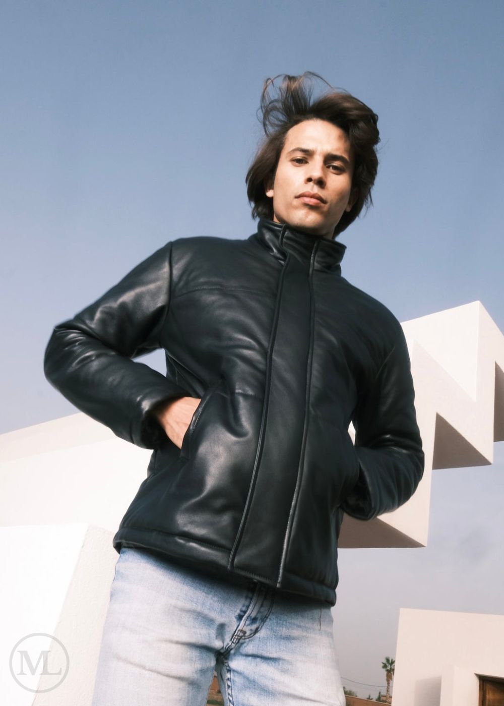 men wearing a black leather down jacket and light blue jeans against a clear sky.