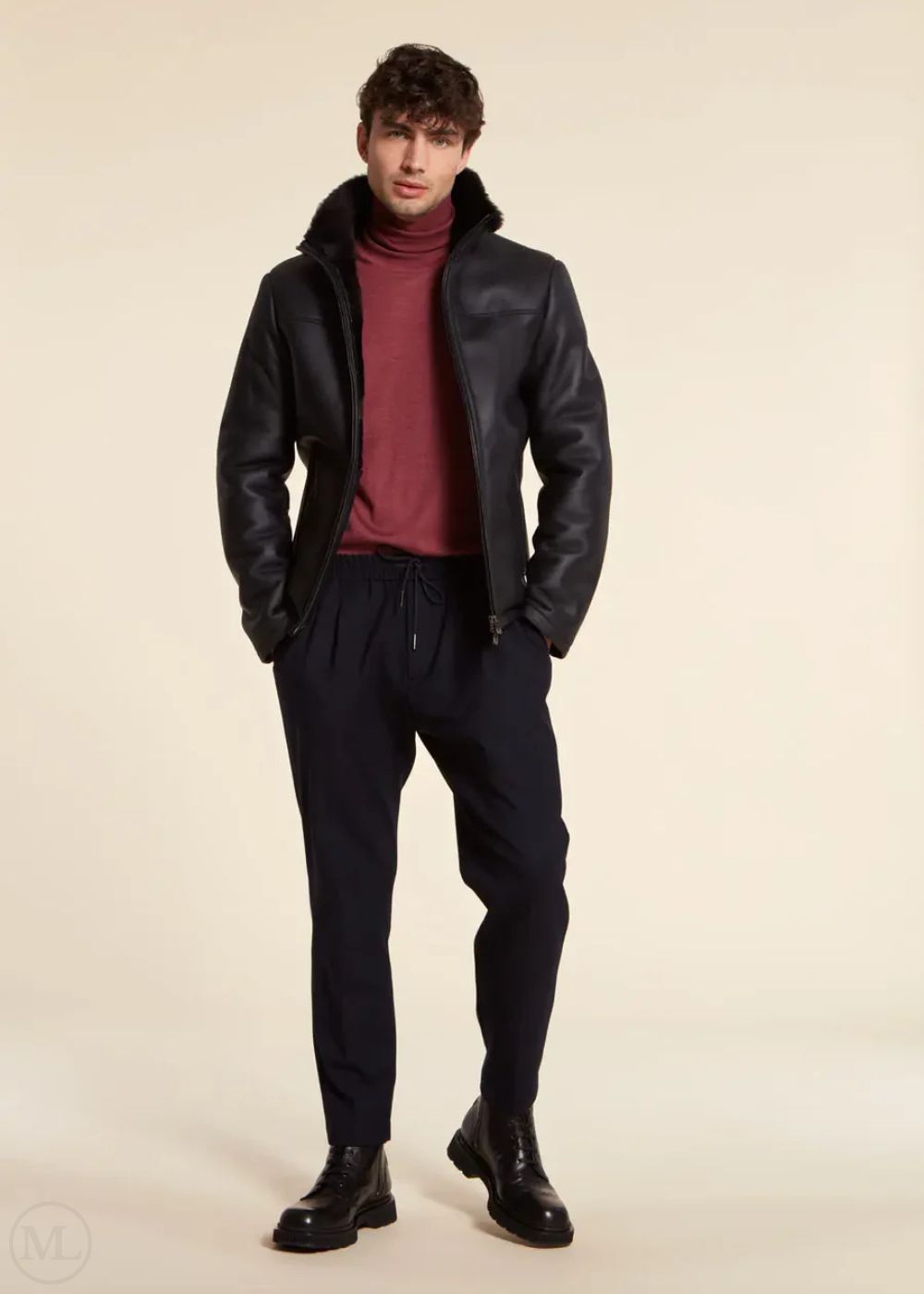 Man wearing a dark blue leather jacket, maroon sweater, and dark pants on a beige background