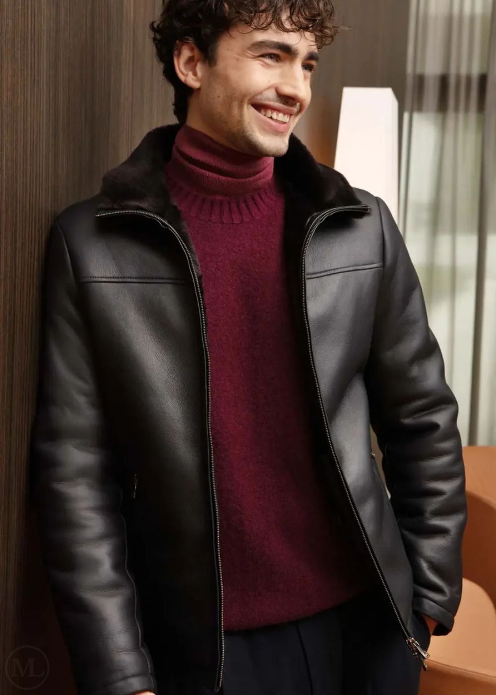 Man wearing a dark blue leather jacket over a red turtleneck sweater indoors.