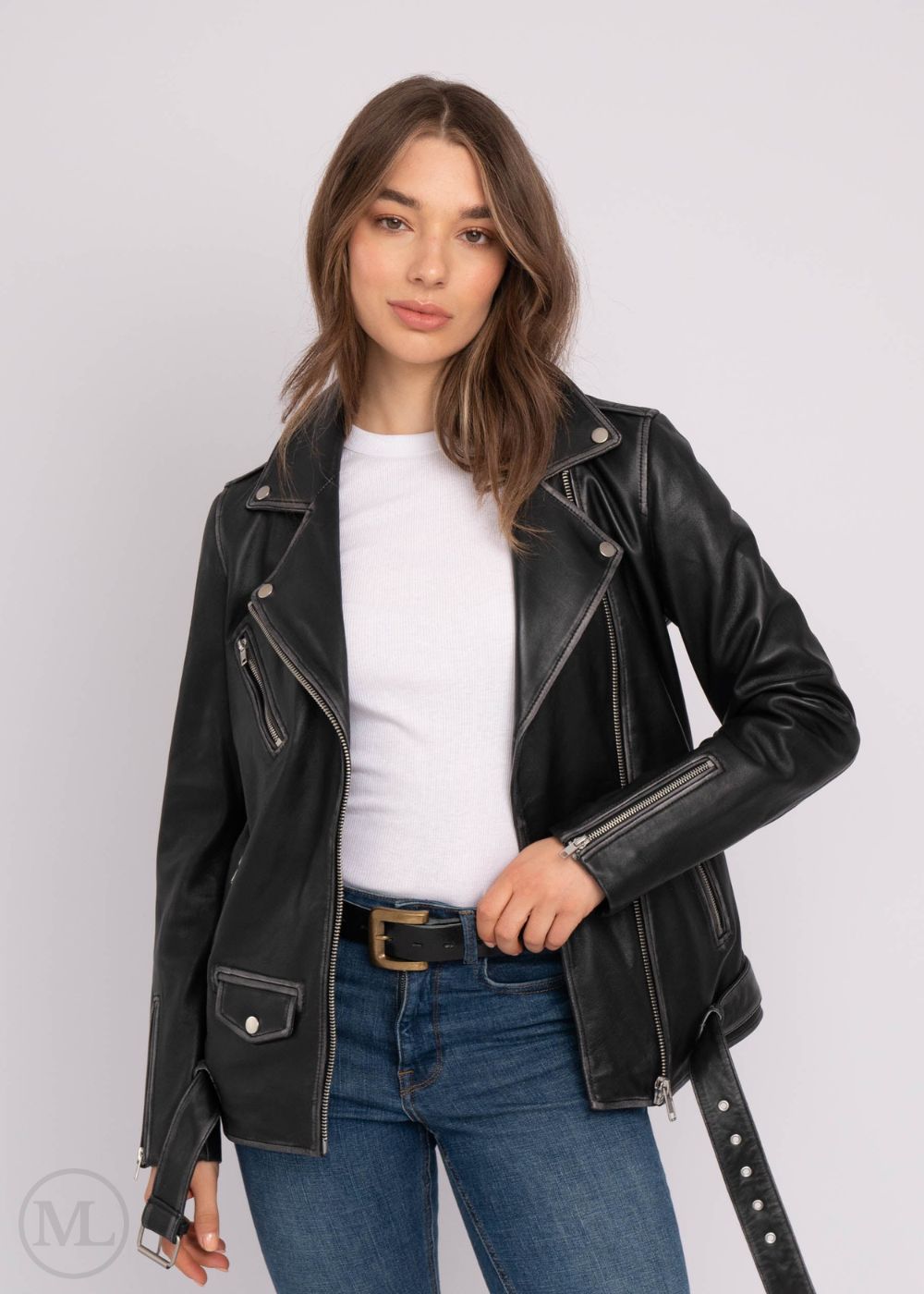 Woman wearing a black leather biker jacket over a white shirt and blue jeans on a light gray background