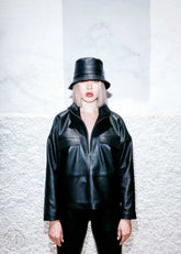 Women wearing a black leather jacket and bucket hat against a textured white background