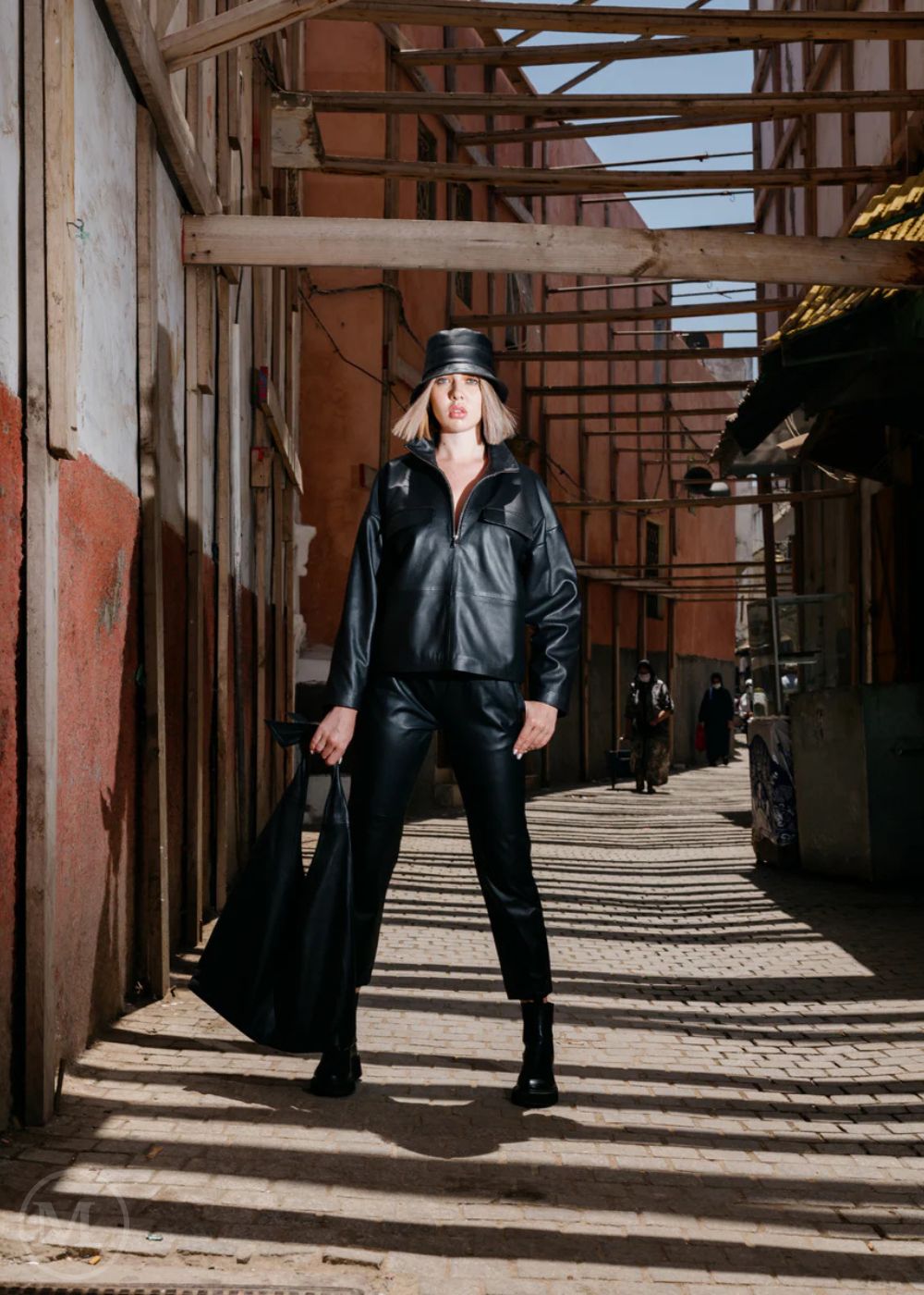 Women in black leather jacket outfit walking through an alleyway with industrial architecture.